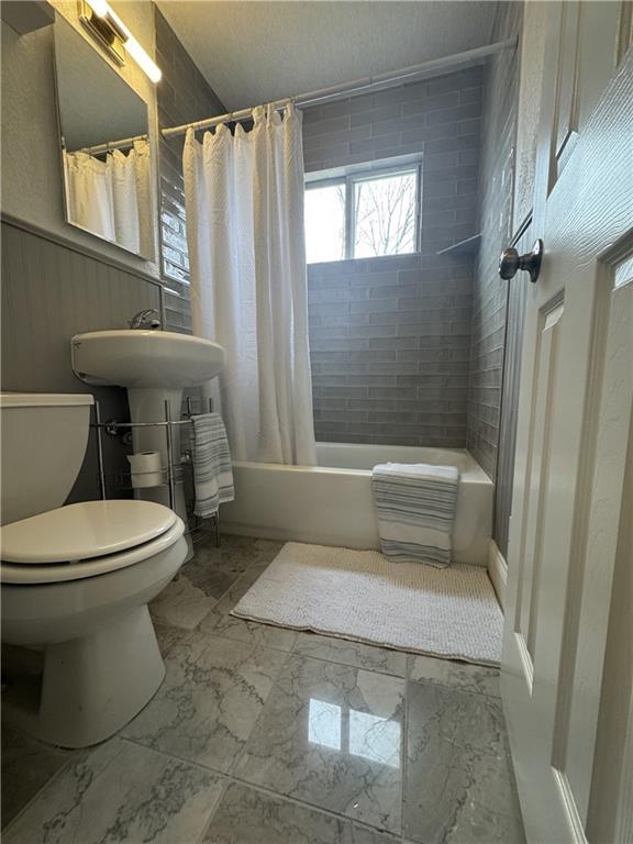 10904 Cambridge Ave, Kansas City, MO 64134 - bathroom with marble finish floor, a wainscoted wall, shower / bathtub combination with curtain, and toilet