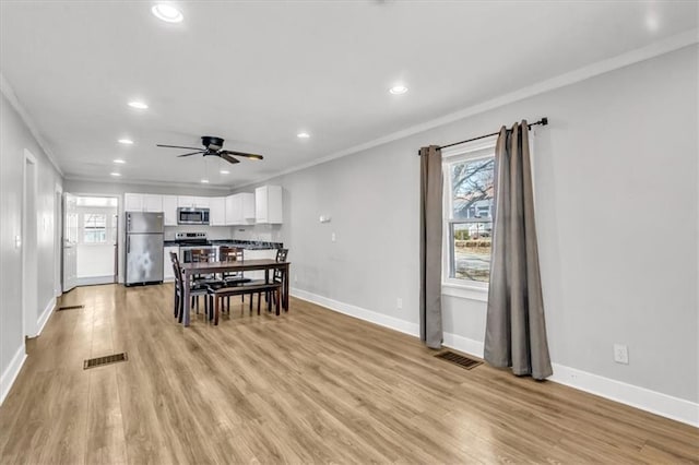 dining area featuring light wood finished floors, visible vents, crown molding, and baseboards