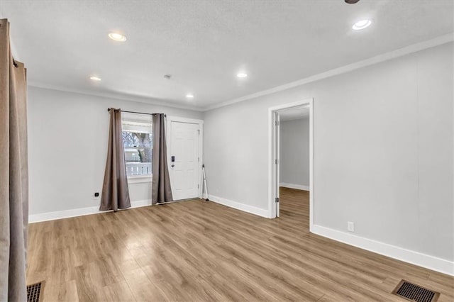 empty room featuring visible vents, baseboards, light wood-style flooring, and crown molding