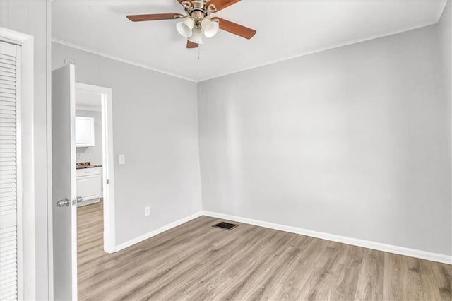 empty room featuring baseboards, visible vents, light wood-type flooring, and ornamental molding