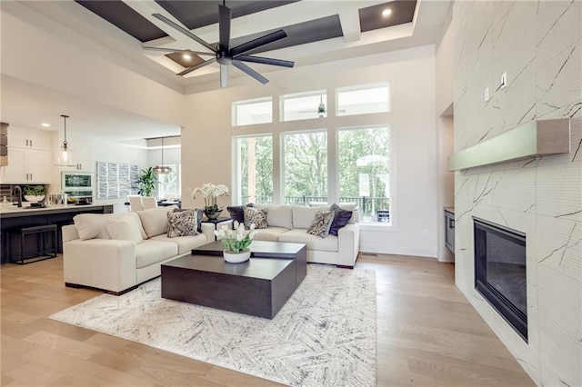 12435 NW Arbor Way, Platte City, MO 64079 - living room featuring a towering ceiling, coffered ceiling, ceiling fan, a high end fireplace, and light wood-type flooring