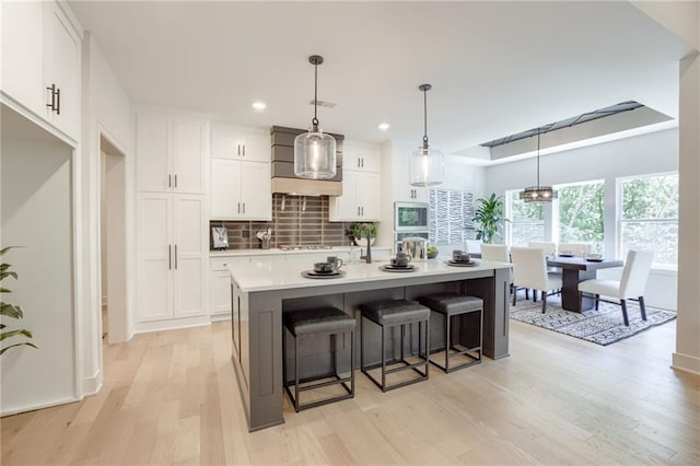 12435 NW Arbor Way, Platte City, MO 64079 - kitchen featuring stainless steel microwave, light wood-style flooring, white cabinets, decorative backsplash, and wall chimney range hood
