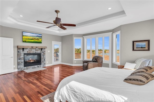 bedroom featuring a stone fireplace, wood finished floors, baseboards, access to outside, and a tray ceiling