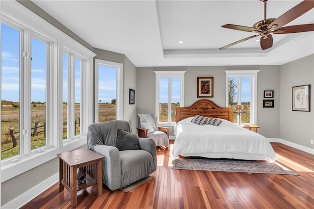 bedroom with a raised ceiling, baseboards, hardwood / wood-style floors, and multiple windows