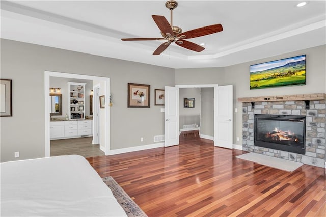 bedroom featuring a raised ceiling, a fireplace, baseboards, and wood finished floors