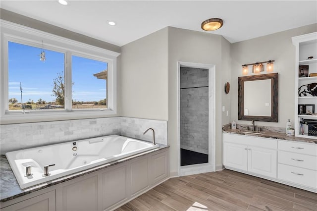 bathroom with wood finished floors, a whirlpool tub, a tile shower, vanity, and recessed lighting