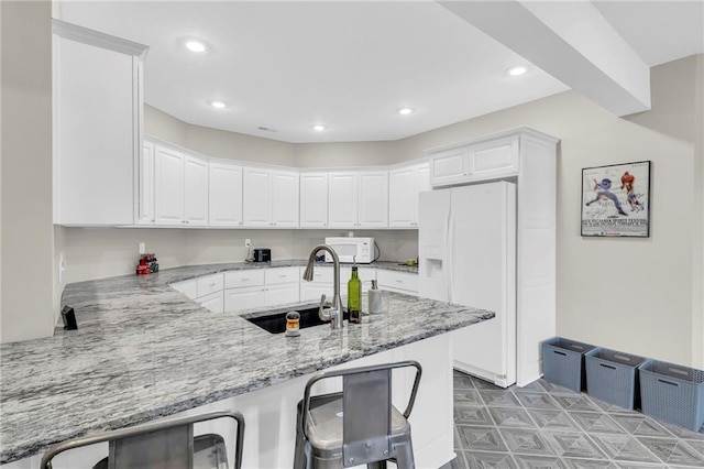 kitchen with white cabinetry, a sink, light stone countertops, white appliances, and a peninsula