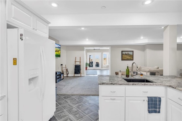 kitchen featuring white refrigerator with ice dispenser, white cabinets, a sink, and open floor plan