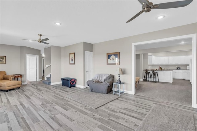 living room with ceiling fan, stairway, baseboards, and light wood finished floors