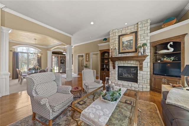 living area featuring decorative columns, wood finished floors, a fireplace, and a chandelier