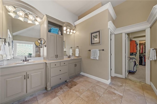 bathroom with double vanity, a walk in closet, baseboards, and a sink