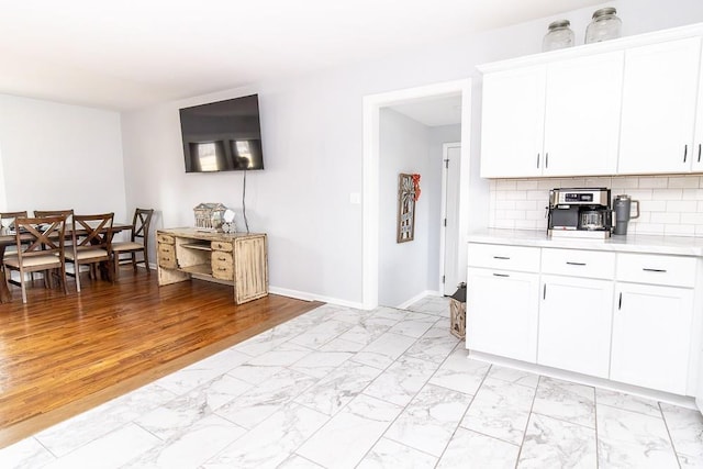 kitchen with marble finish floor, light countertops, decorative backsplash, white cabinets, and baseboards