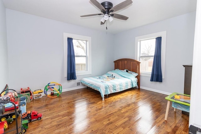 bedroom with a ceiling fan, visible vents, baseboards, and wood finished floors