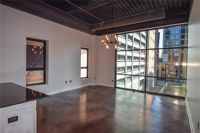 unfurnished dining area with a healthy amount of sunlight, finished concrete flooring, baseboards, and an inviting chandelier