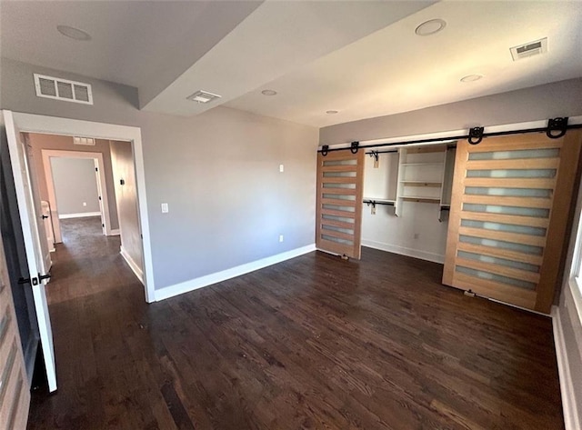 unfurnished bedroom with a barn door, dark wood-type flooring, and visible vents