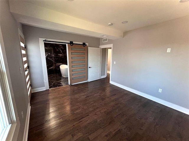 unfurnished bedroom with a spacious closet, wood finished floors, visible vents, and baseboards