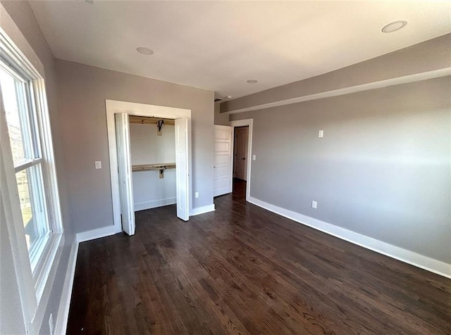 unfurnished bedroom featuring dark wood-type flooring, multiple windows, and baseboards