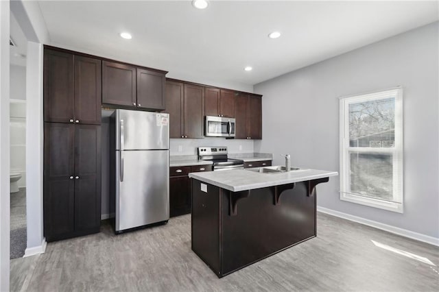 kitchen with dark brown cabinetry, stainless steel appliances, light countertops, light wood finished floors, and an island with sink