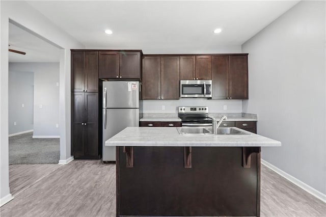 kitchen featuring an island with sink, dark brown cabinetry, appliances with stainless steel finishes, and light countertops