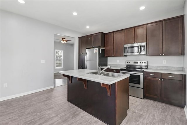 kitchen featuring dark brown cabinetry, a breakfast bar, a sink, light countertops, and appliances with stainless steel finishes