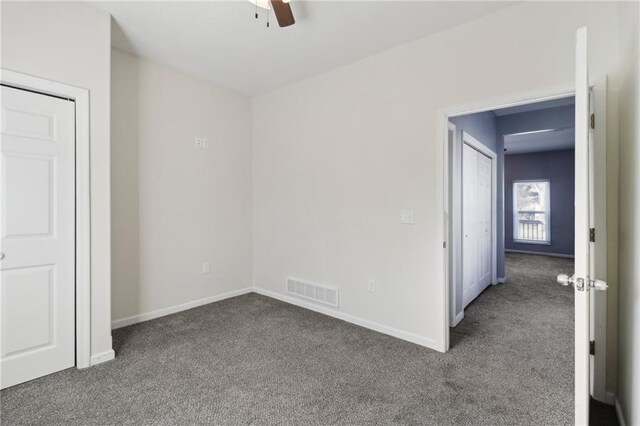 unfurnished bedroom with a ceiling fan, visible vents, dark carpet, and baseboards