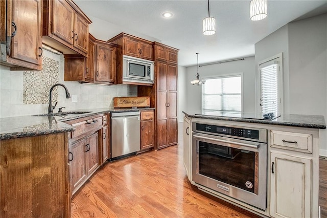 kitchen with a sink, tasteful backsplash, dark stone counters, light wood-style floors, and appliances with stainless steel finishes