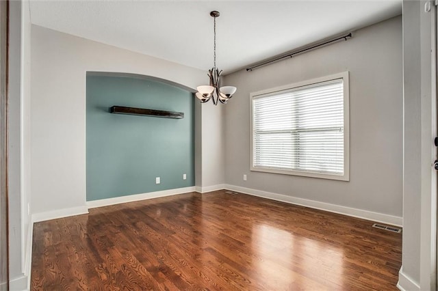 empty room with arched walkways, visible vents, dark wood-style flooring, and baseboards