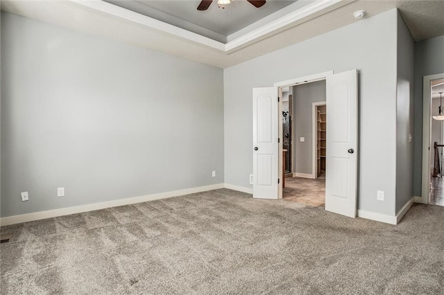 unfurnished bedroom with carpet flooring, ceiling fan, a raised ceiling, and baseboards