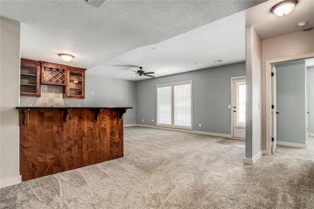 kitchen with dark countertops, glass insert cabinets, baseboards, light carpet, and a peninsula