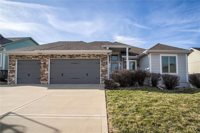 view of front of house with a shingled roof, a front lawn, concrete driveway, a garage, and stone siding