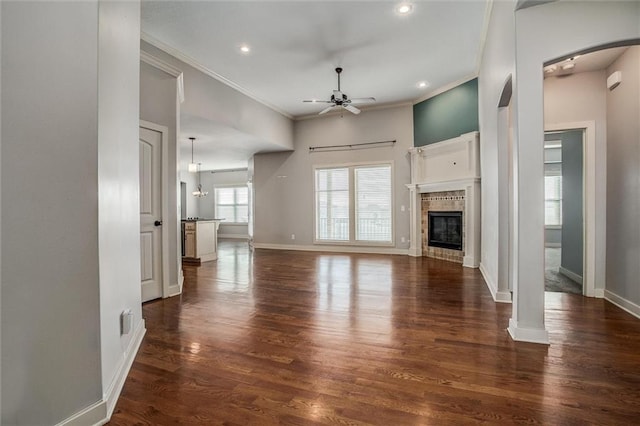 unfurnished living room featuring baseboards, a tiled fireplace, ornamental molding, wood finished floors, and a ceiling fan