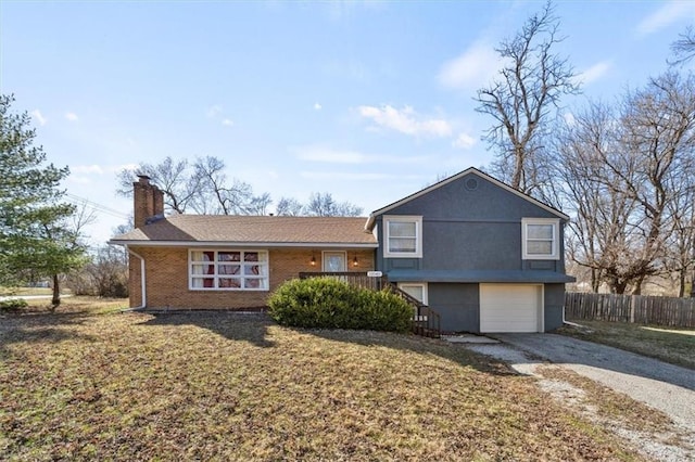 split level home with an attached garage, a front lawn, fence, a chimney, and driveway