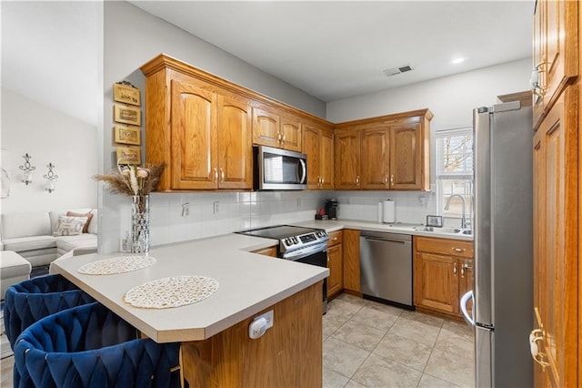 kitchen featuring stainless steel appliances, backsplash, a sink, and a peninsula