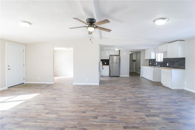 kitchen featuring tasteful backsplash, open floor plan, wood finished floors, freestanding refrigerator, and white cabinetry