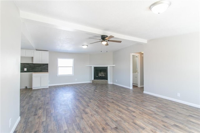 unfurnished living room featuring a fireplace with raised hearth, ceiling fan, wood finished floors, beamed ceiling, and baseboards