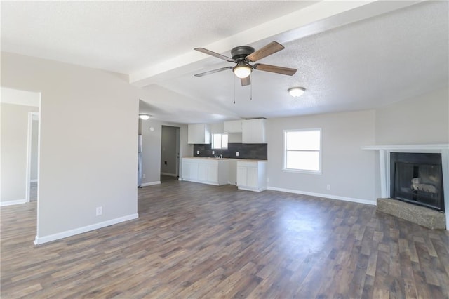 unfurnished living room with ceiling fan, baseboards, dark wood finished floors, and beam ceiling