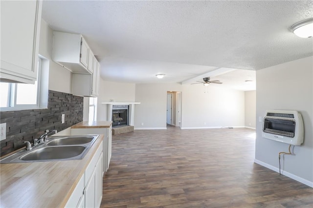 kitchen with a fireplace with raised hearth, a sink, white cabinets, open floor plan, and heating unit