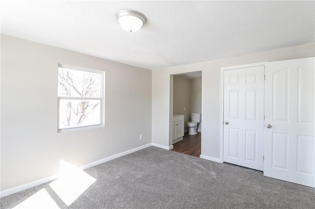 unfurnished bedroom featuring dark carpet, a textured ceiling, baseboards, and ensuite bathroom