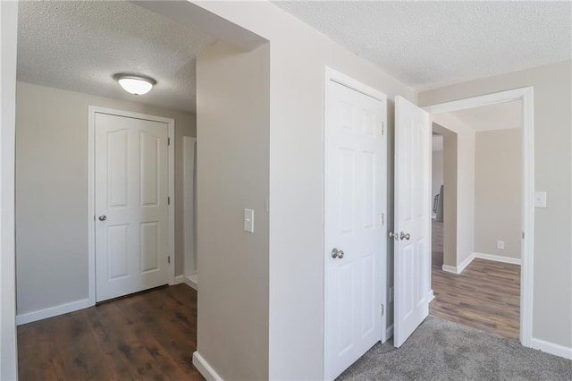 hallway with a textured ceiling, baseboards, and wood finished floors