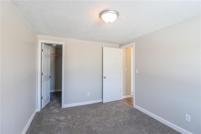 unfurnished bedroom featuring carpet, a closet, a spacious closet, a textured ceiling, and baseboards