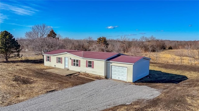 view of front facade with an attached garage, metal roof, and gravel driveway