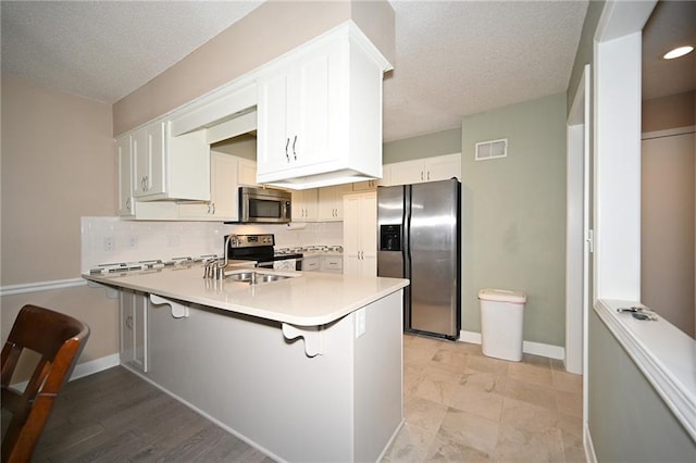 kitchen featuring stainless steel appliances, a peninsula, a sink, visible vents, and backsplash