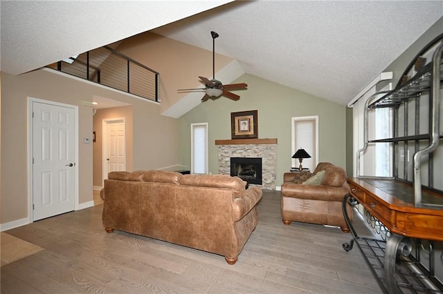 living area featuring a stone fireplace, ceiling fan, light wood-style flooring, and baseboards