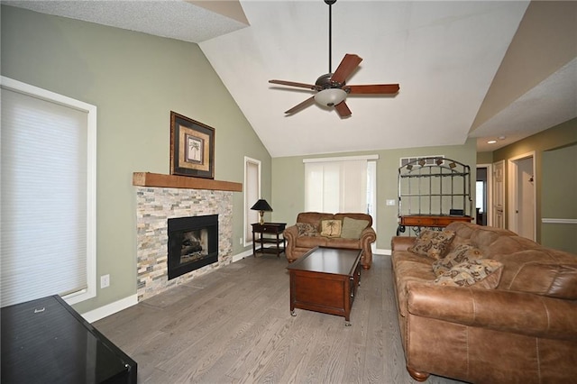 living room featuring high vaulted ceiling, a stone fireplace, a ceiling fan, baseboards, and light wood finished floors