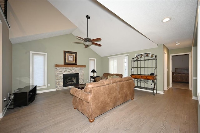 living room with lofted ceiling, light wood-type flooring, a stone fireplace, and baseboards