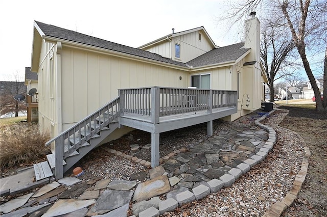 back of property with roof with shingles, a chimney, central AC unit, a deck, and stairs