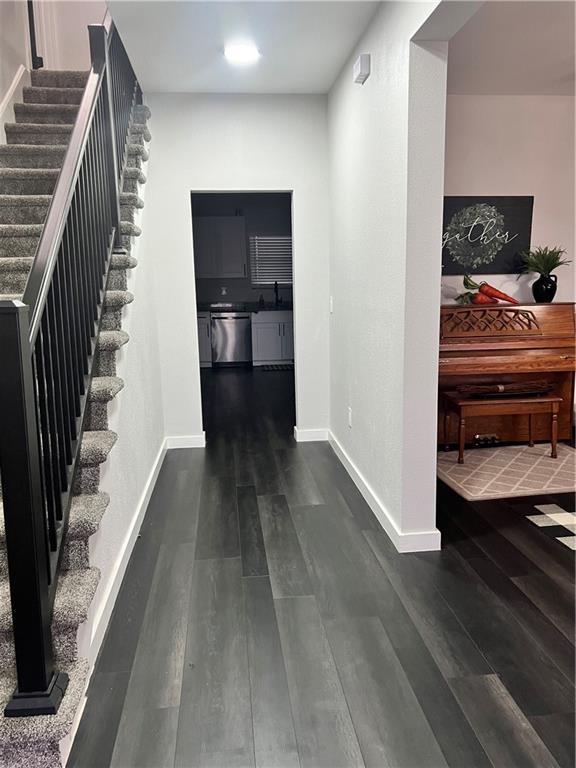 hall featuring dark wood-style floors, stairs, baseboards, and a sink