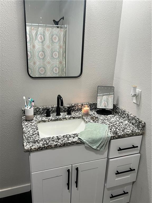 full bathroom featuring curtained shower, a textured wall, vanity, and baseboards