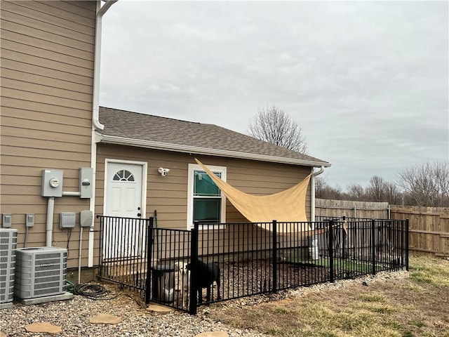 exterior space with fence, central AC unit, and roof with shingles