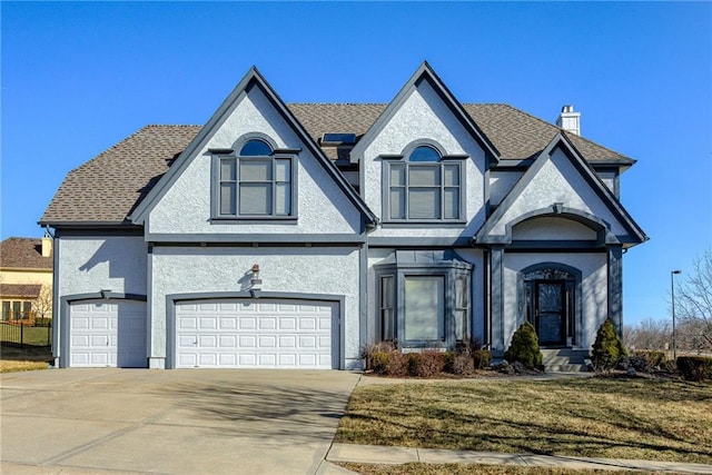 french provincial home with concrete driveway, stucco siding, a garage, and a chimney